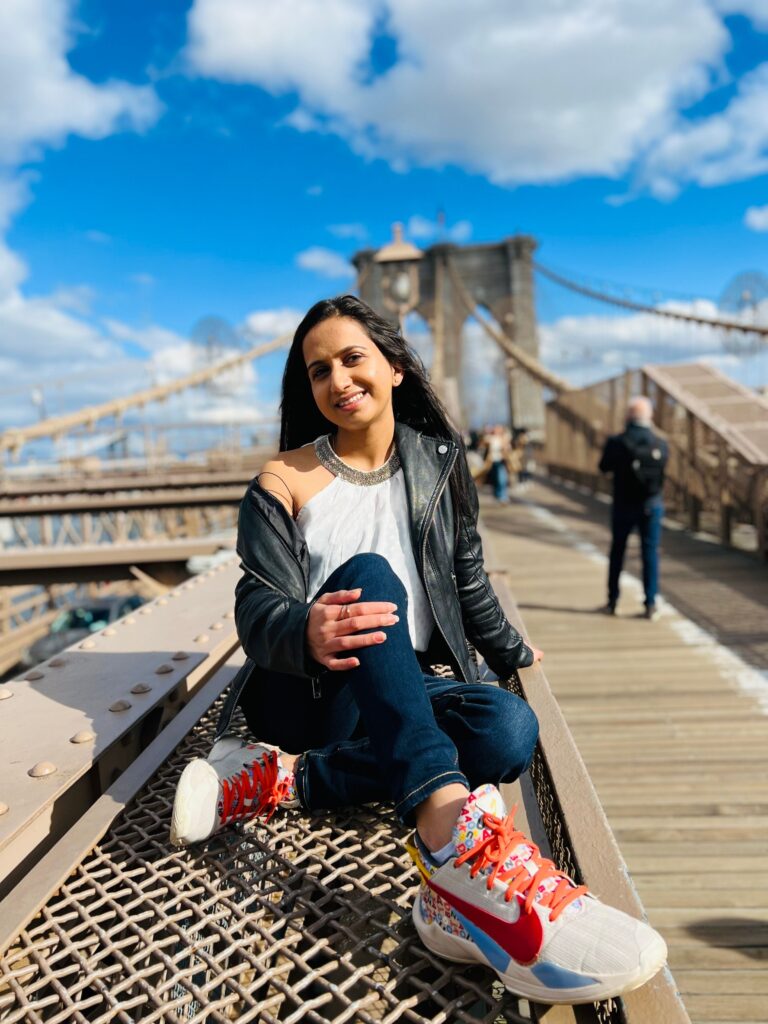 Dippan sitting on Brooklyn Bridge walkway with Manhattan skyline in the background on a sunny day