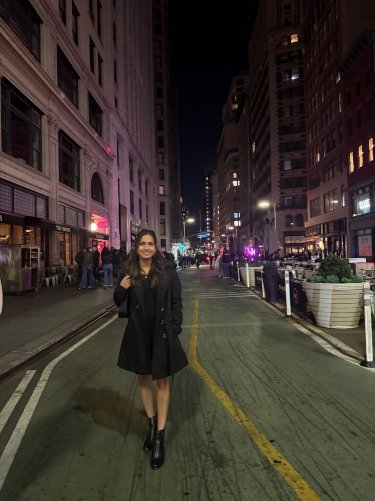 Dippan walking through New York City streets at night surrounded by tall buildings