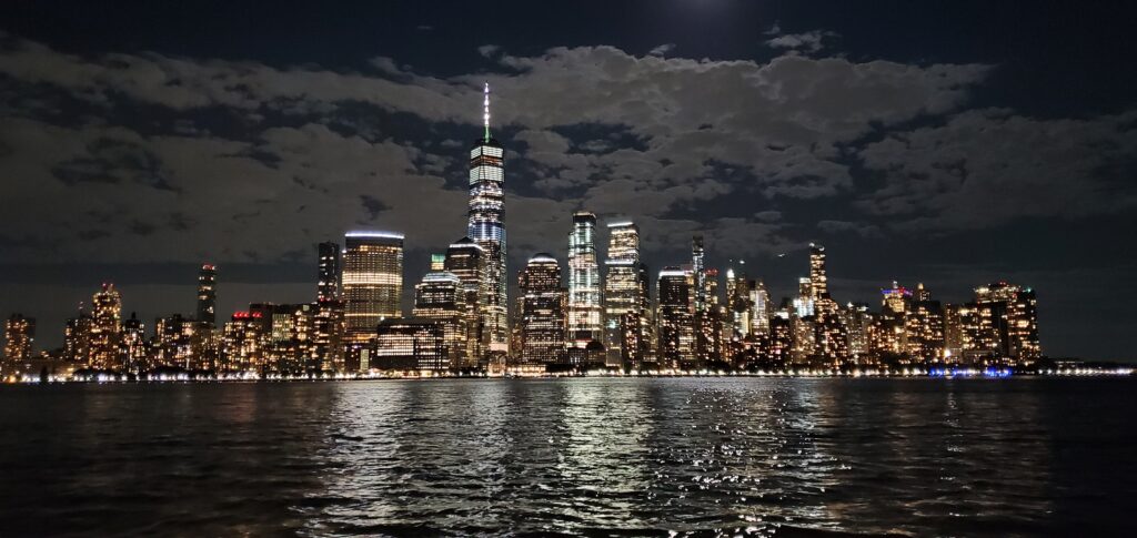 New York City skyline at night viewed from the waterfront with city lights reflecting on the river
