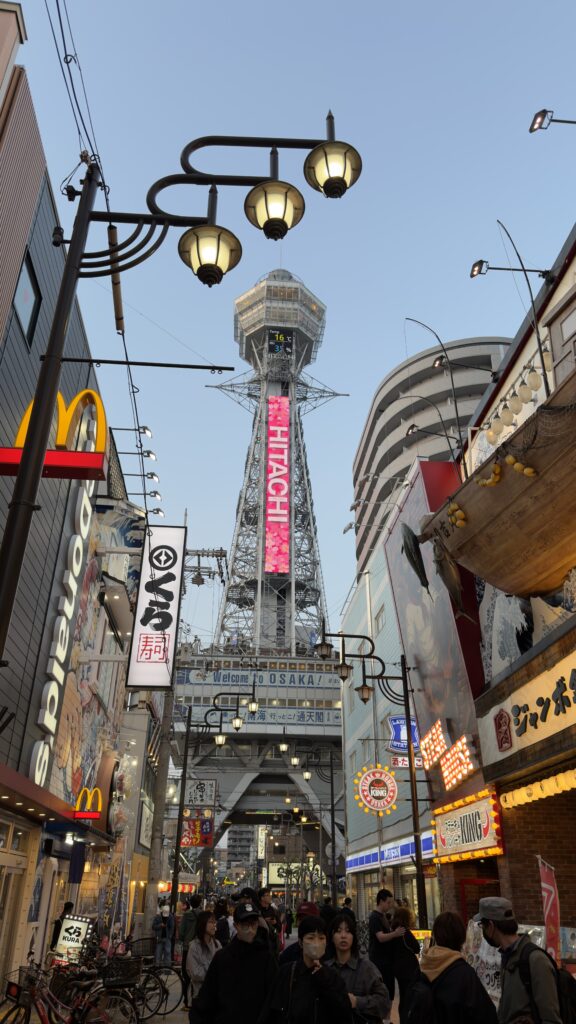 Tsutenkaku Tower rising above a busy shopping street lined with neon signs and shop fronts in Shinsekai, Osaka
