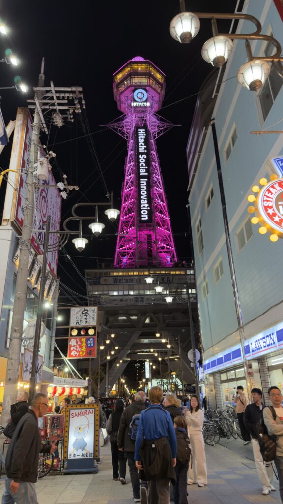 Tsutenkaku Tower illuminated in pink at night above a crowded Shinsekai shopping street, Osaka