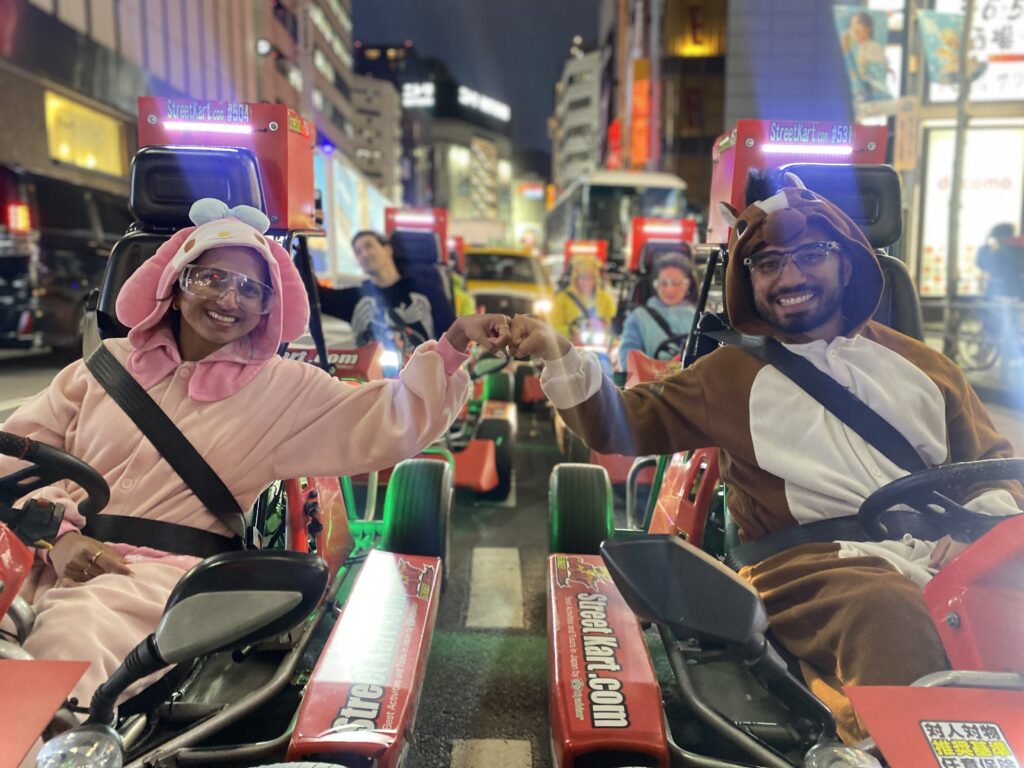 Two people in animal onesies driving street karts at night in Tokyo